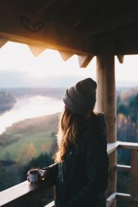 Jeune femme en train de boire son café sur le balcon de son chalet de montagne